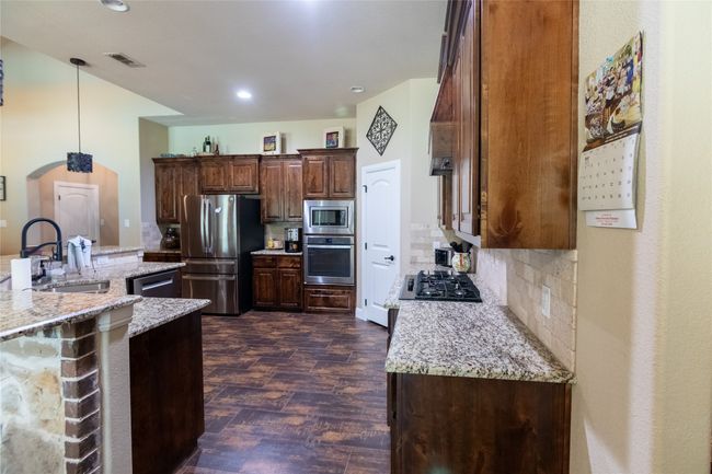 Kitchen featuring stainless steel appliances, a sink, dark wood-style floors, tasteful backsplash, and light stone countertops | Image 15