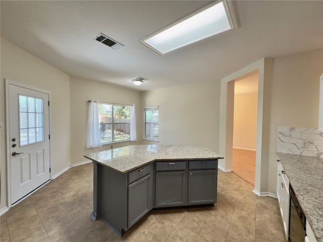 Kitchen featuring gray cabinets, light tile patterned floors, a kitchen island, and light stone counters | Image 7