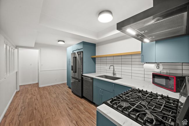 Kitchen with wall chimney exhaust hood, stainless steel appliances, blue cabinets, a sink, and light wood-style flooring | Image 9