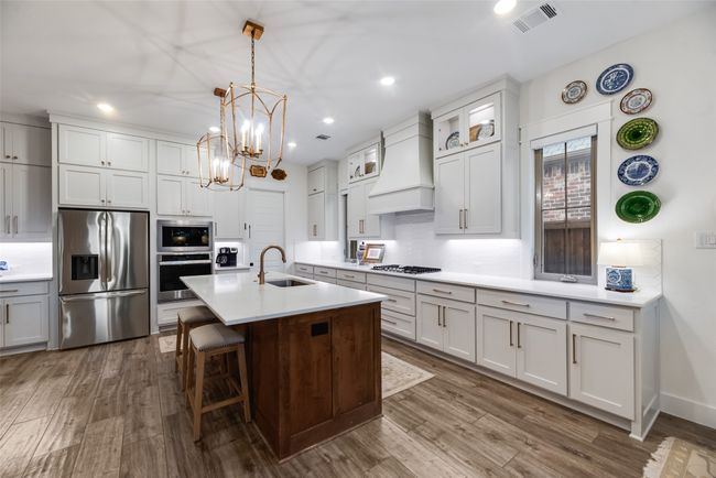 Kitchen with appliances with stainless steel finishes, custom exhaust hood, a sink, dark wood finished floors, and a kitchen breakfast bar | Image 14