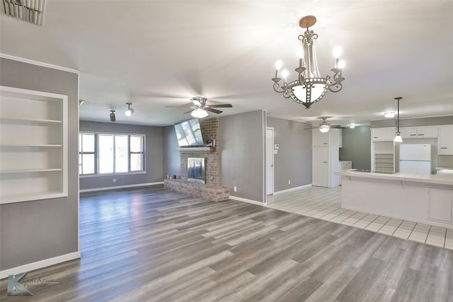 Unfurnished living room featuring a fireplace, ceiling fan with notable chandelier, light hardwood / wood-style floors, and built in features | Image 7