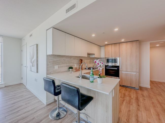 Kitchen with stainless steel microwave, oven, modern cabinets, a kitchen breakfast bar, and light countertops | Image 7