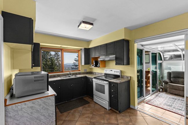 Kitchen featuring under cabinet range hood, electric stove, a sink, and dark cabinetry | Image 11