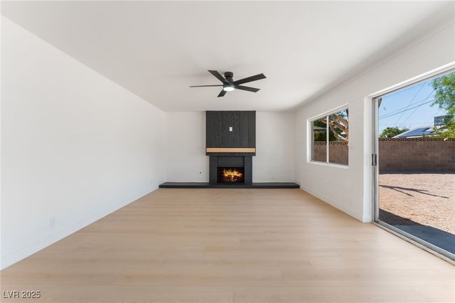 Unfurnished living room featuring light wood finished floors, healthy amount of natural light, ceiling fan, and a fireplace | Image 10