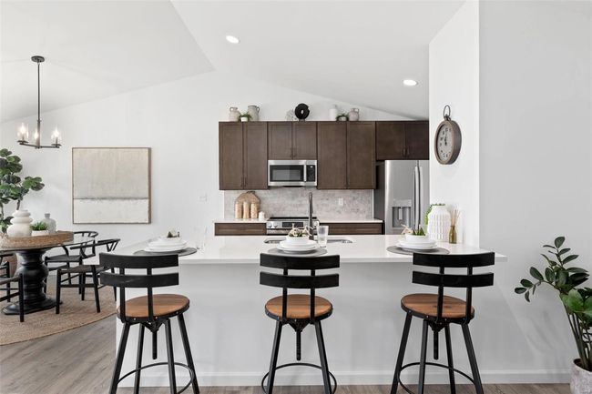 Kitchen featuring appliances with stainless steel finishes, hanging light fixtures, a breakfast bar, light wood-type flooring, and dark brown cabinetry | Image 17