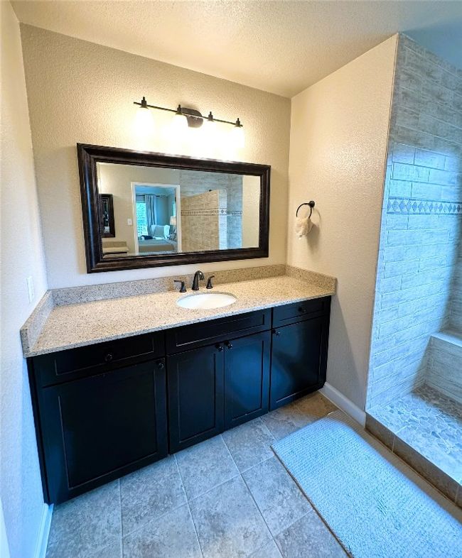Primary Bathroom with a textured wall, dual vanities, a textured ceiling, a tile shower, and tile patterned floors. | Image 28