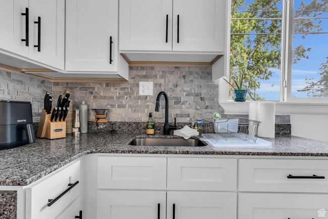 Kitchen featuring a sink, decorative backsplash, white cabinetry, and stone countertops | Image 6