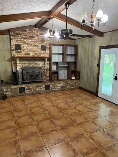 Unfurnished living room featuring brick wall, tile flooring, a textured ceiling, and a fireplace | Image 2