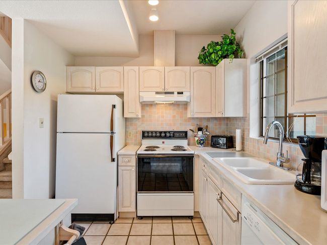 Kitchen with white appliances, tasteful backsplash, under cabinet range hood, and a sink | Image 13