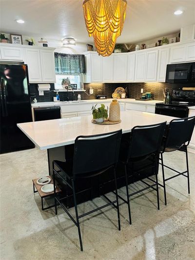 Kitchen with decorative backsplash, a kitchen island, a breakfast bar area, black appliances, and white cabinetry | Image 2