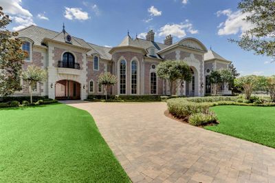 This is a grand, two-story brick home featuring a symmetrical facade with an arched entryway, large windows, and a manicured lawn. It offers a luxurious and stately appearance, complete with a curved driveway and elegant landscaping. | Image 2