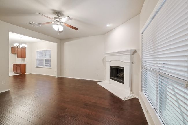 Unfurnished living room featuring a chandelier, ceiling fan, a fireplace with raised hearth, and dark wood-type flooring | Image 7
