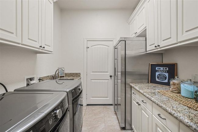 Conveniently adjacent to the kitchen, this well-appointed laundry room offers a utility sink, room for a secondary fridge, a dedicated folding area, and generous cabinet storage. Washer and dryer are included. | Image 28