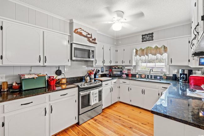 Kitchen with appliances with stainless steel finishes, crown molding, a textured ceiling, white cabinetry, and a ceiling fan | Image 4
