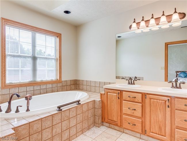 Primary Bathroom featuring a relaxing tiled bath, double sink vanity, a textured ceiling, light tile flooring, and mirror | Image 7