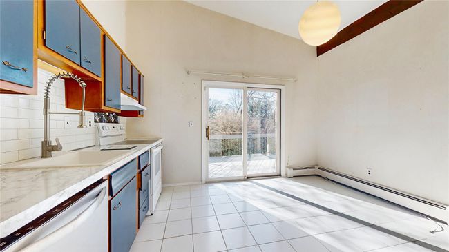 Kitchen featuring blue cabinets, tasteful backsplash, white appliances, light countertops, and baseboard heating | Image 9