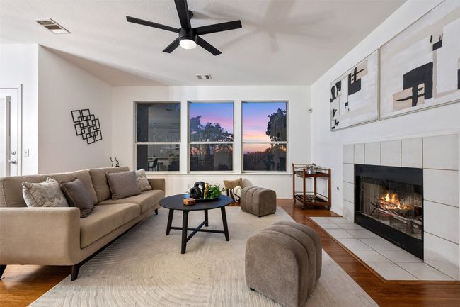 Living room with wood finished floors, ceiling fan, a fireplace, and visible vents | Image 4