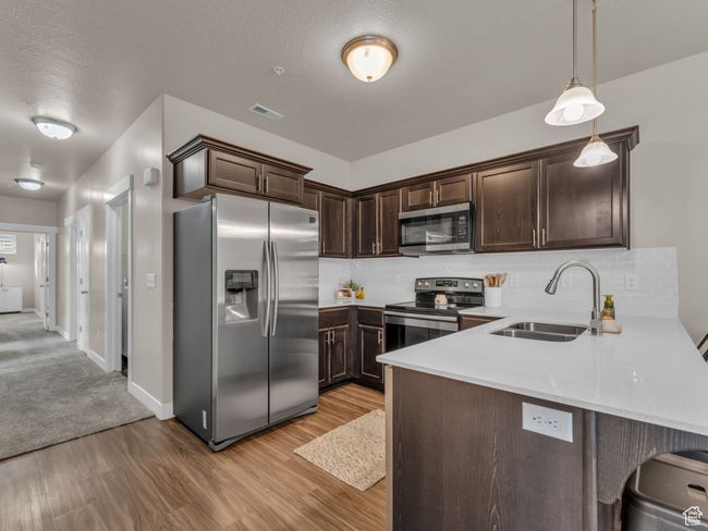 Kitchen featuring appliances with stainless steel finishes, a sink, dark brown cabinetry, light wood-style flooring, and tasteful backsplash | Image 7
