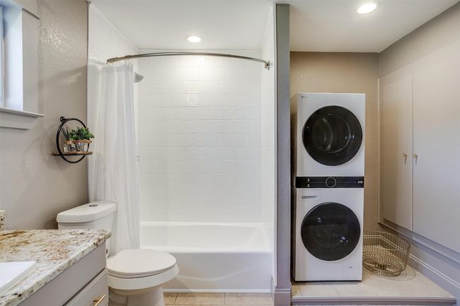 Full bathroom with stacked washing machine and dryer, vanity, shower / bathtub combination with curtain, toilet, and recessed lighting | Image 23
