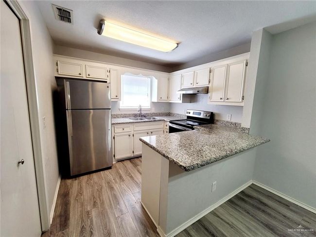 Kitchen with appliances with stainless steel finishes, under cabinet range hood, light wood-style floors, a peninsula, and white cabinets | Image 10