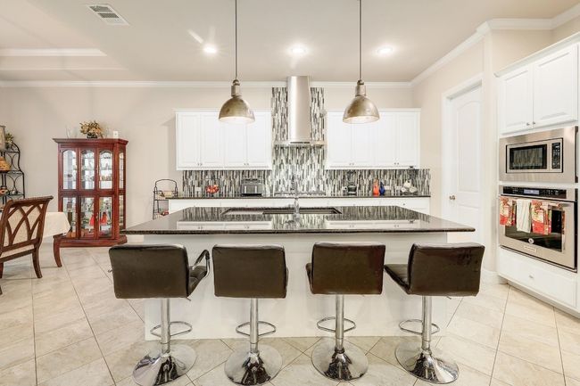 Kitchen with light tile patterned floors, crown molding, a breakfast bar, stainless steel appliances, and backsplash | Image 11