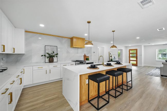 Kitchen featuring stainless steel range with gas stovetop, decorative backsplash, light wood-style flooring, a kitchen breakfast bar, and recessed lighting | Image 9