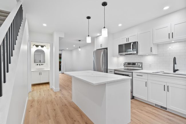 Kitchen featuring a kitchen island, stainless steel appliances, light wood-style floors, and a sink | Image 7