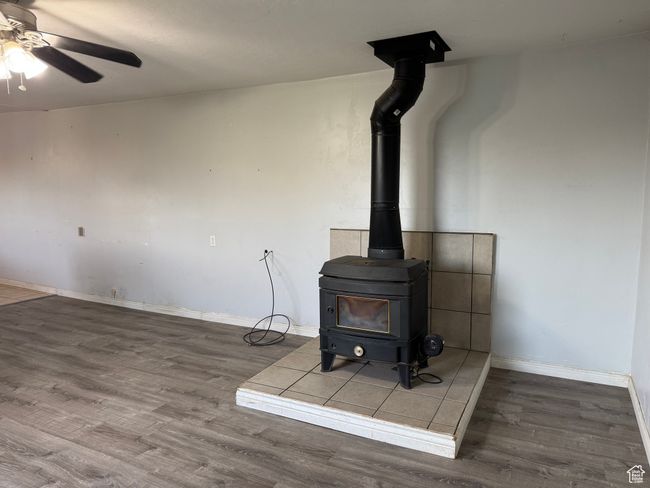 Detailed view of a wood stove, wood finished floors, ceiling fan, and baseboards | Image 5