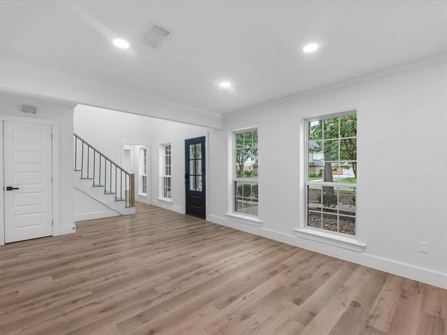 Bright and airy living space with large windows, wood flooring, and a modern staircase. The open layout and neutral colors create an inviting atmosphere. | Image 6