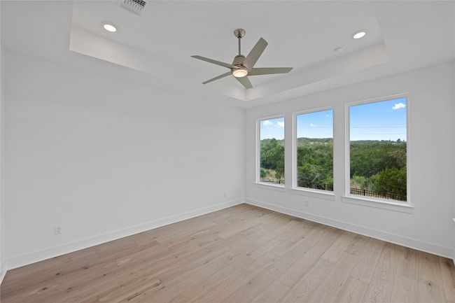 Empty room featuring a raised ceiling, baseboards, light wood-type flooring, ceiling fan, and recessed lighting | Image 13