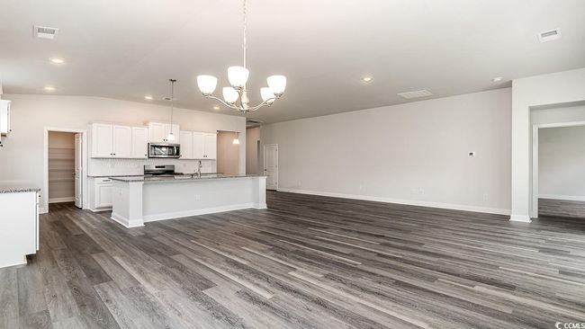 Kitchen featuring stove, white cabinets, a center island with sink, hanging light fixtures, and wood-type flooring | Image 18
