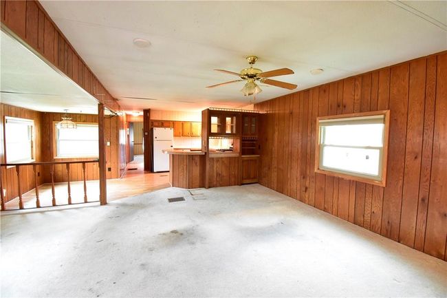Unfurnished living room featuring wood walls, ceiling fan, light colored carpet, and plenty of natural light | Image 27