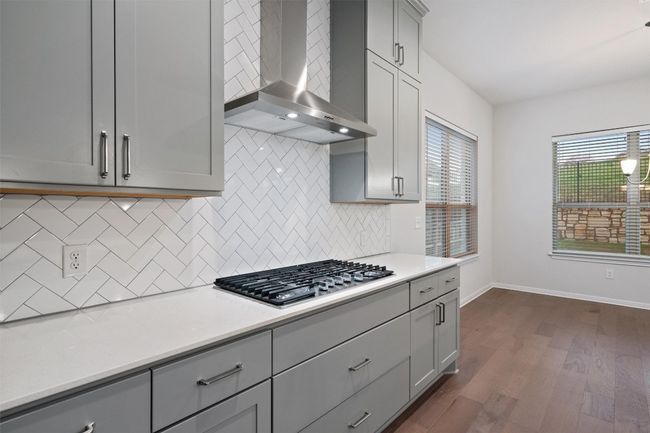 Kitchen featuring gray cabinets, dark wood finished floors, stainless steel gas cooktop, and wall chimney exhaust hood | Image 14