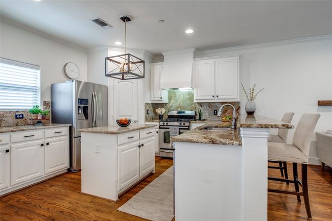 Kitchen featuring appliances with stainless steel finishes, custom exhaust hood, ornamental molding, a breakfast bar, and decorative backsplash | Image 10