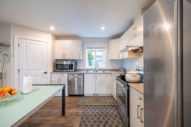 Kitchen with backsplash, under cabinet range hood, light countertops, stainless steel appliances, and a sink | Image 10