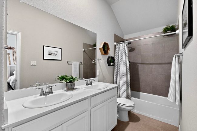 Ensuite bathroom with shower / bath combo with shower curtain, lofted ceiling, double vanity, and light tile patterned floors | Image 33