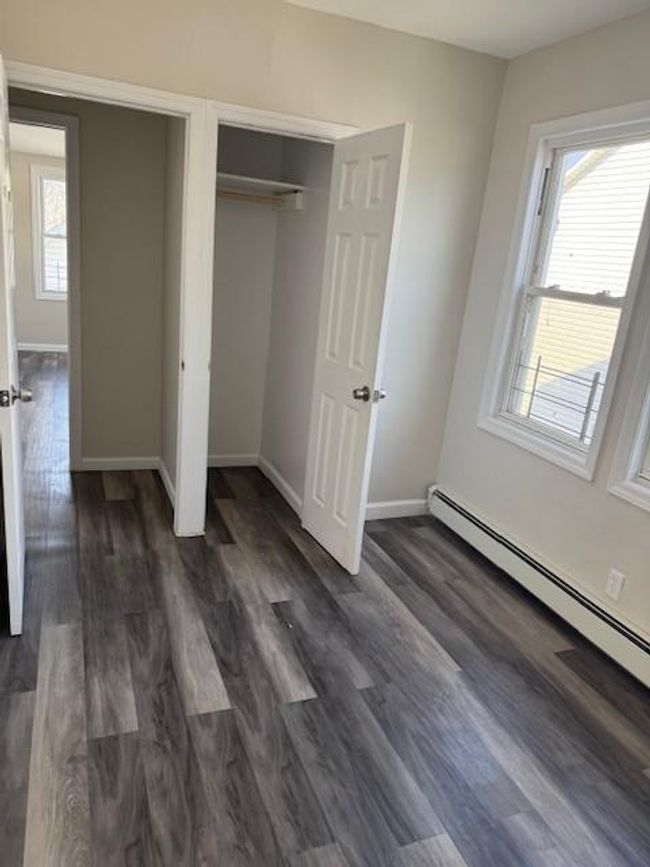Unfurnished bedroom featuring baseboard heating, dark wood-style floors, and a closet | Image 13