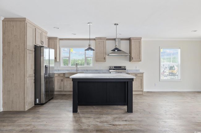 Kitchen featuring stainless steel appliances, light brown cabinetry, wall chimney exhaust hood, light countertops, and crown molding | Image 12