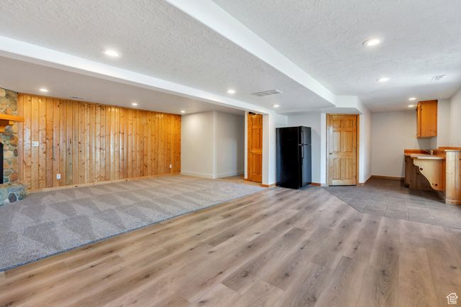 Unfurnished living room with a textured ceiling, baseboards, light wood finished floors, wooden walls, and recessed lighting | Image 17
