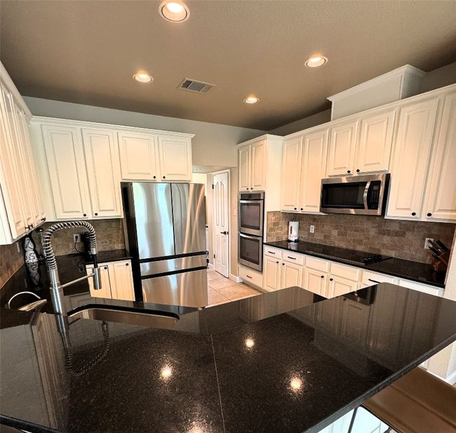 Kitchen featuring appliances with stainless steel finishes, recessed lighting, white cabinets, backsplash, and a breakfast bar area. | Image 8
