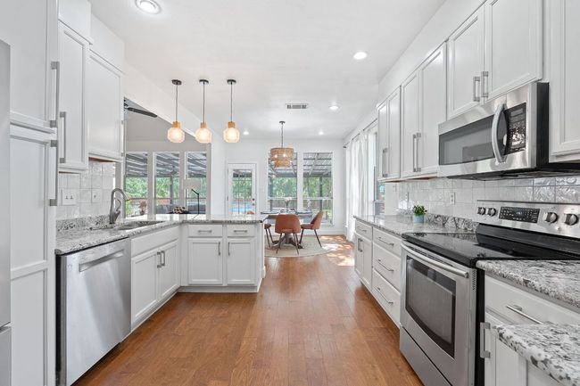 Kitchen featuring appliances with stainless steel finishes, a peninsula, wood finished floors, white cabinets, and recessed lighting | Image 8