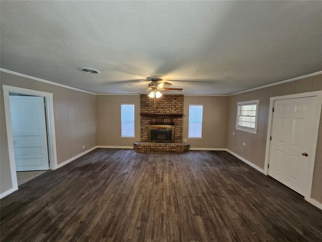 Unfurnished living room with a fireplace, crown molding, a ceiling fan, and dark wood-style flooring | Image 11
