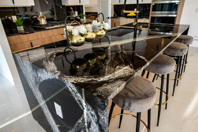 Experience luxury at its finest with this striking kitchen centerpiece—a waterfall-edge island crafted from dramatic, high-gloss black granite featuring intricate natural veining. The rich, polished stone extends seamlessly to the floor, creating a bold, sculptural statement. Complemented by sleek fixtures and exquisite craftsmanship, this space epitomizes modern elegance and attention to detail. | Image 12