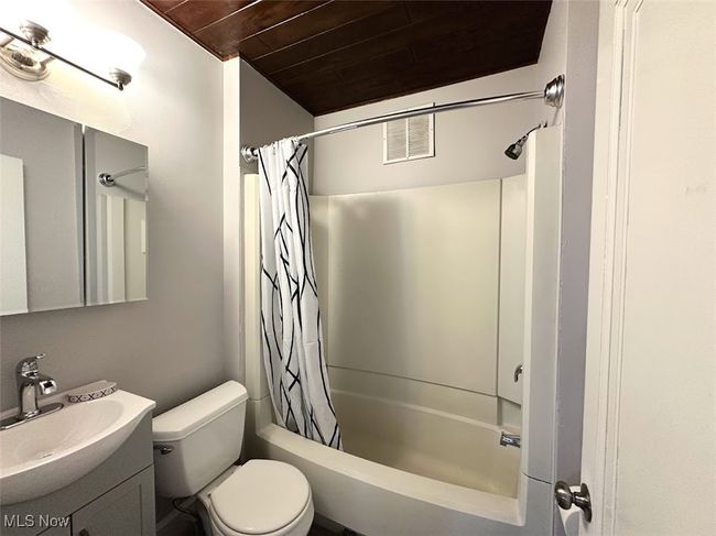 Full bath featuring visible vents, wooden ceiling, toilet, shower / bathtub combination with curtain, and vanity | Image 4