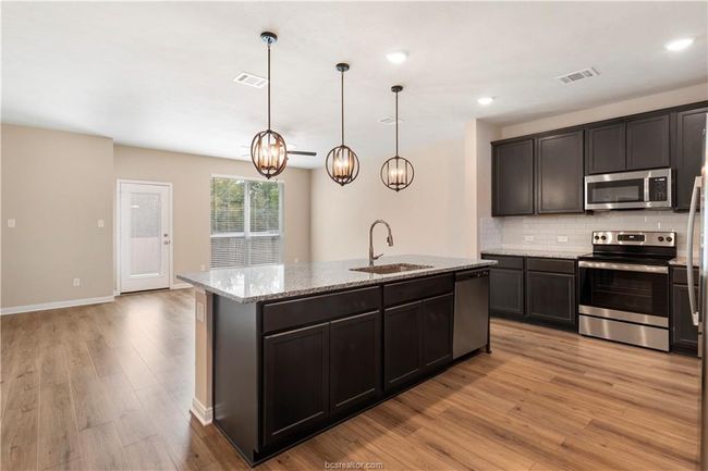 Kitchen featuring stainless steel appliances, decorative backsplash, a kitchen island with sink, light wood finished floors, and light stone counters | Image 7