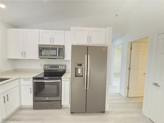 Kitchen featuring stainless steel appliances, vaulted ceiling, white cabinets, light wood-style flooring, and light countertops | Image 10