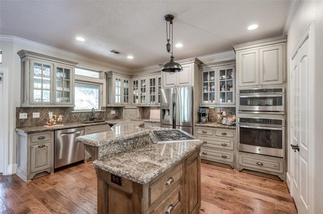 Discover a beautifully equipped kitchen featuring elegant glass-front cabinets, granite countertops, and under-cabinet lighting. Enjoy modern conveniences like a touch-free faucet, RO system, gas stovetop with retractable vent, and a Wi-Fi enabled convection oven. The microwave doubles as a second oven, complemented by a spacious walk-in pantry and abundant storage. Major appliances, including the oven, microwave, and dishwasher, were updated in 2018. | Image 11