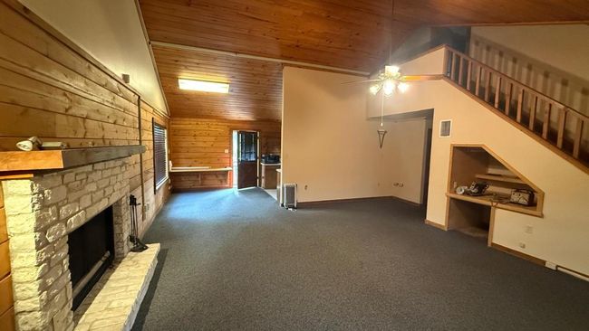 Unfurnished living room with lofted ceiling, wood ceiling, visible vents, wooden walls, and a ceiling fan | Image 9