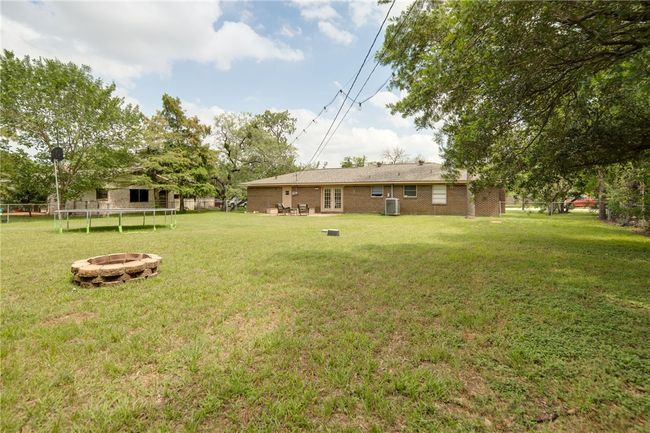View of green lawn featuring a fire pit, a trampoline, an outdoor structure, and central AC unit | Image 22