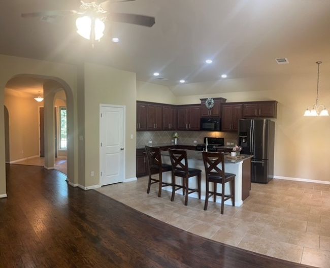 Kitchen featuring fridge with ice dispenser, black microwave, arched walkways, ceiling fan, and backsplash | Image 10